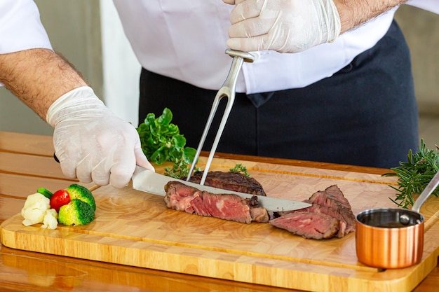 mano uomo taglio bistecca di carne, affettare succosa bistecca di manzo con un coltello nelle mani dello chef primo piano. Cottura del cibo