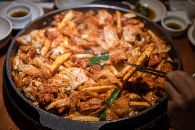 Mano usando le bacchette per raccogliere il pollo al barbecue Dakgalbi con verdure mescolate in padella calda