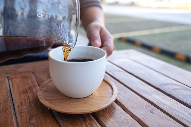 mano versando il caffè a goccia in una tazza bianca sul tavolo in legno d'epoca