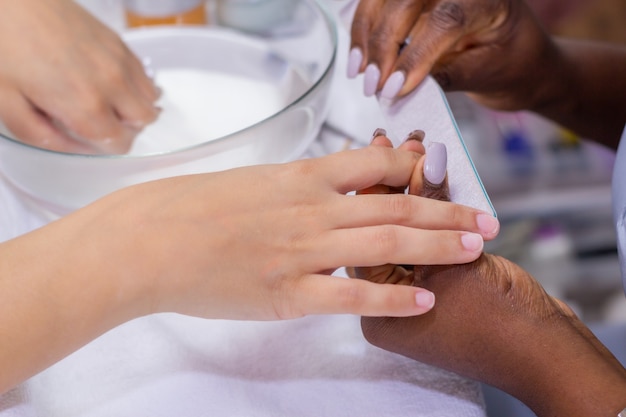 Manos manicuristas aplicando las unas del cliente femenino con un tampon blanco en el salon de unas