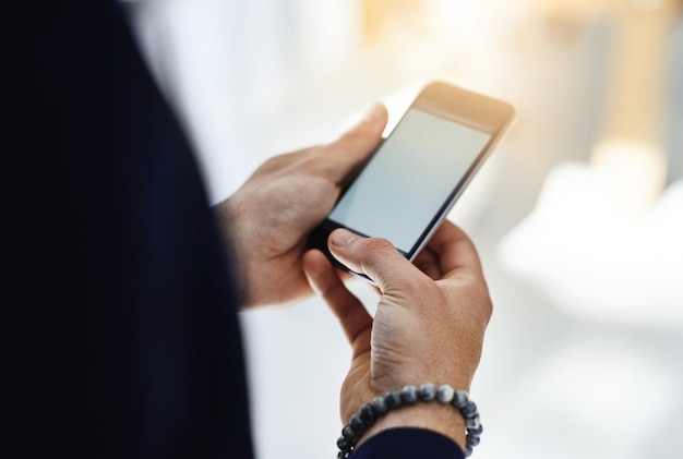 Mantenere la mobilità aziendale Foto ritagliata di un uomo d'affari che utilizza un telefono cellulare in un ufficio moderno