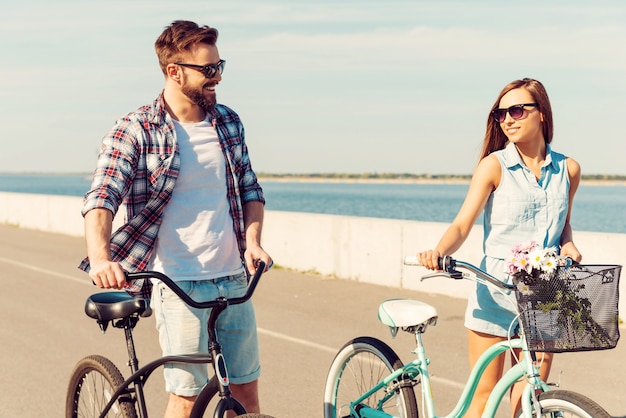 Mantenersi in forma e divertirsi. Felice giovane coppia che fa rotolare le biciclette e si guarda con un sorriso mentre cammina all'aperto