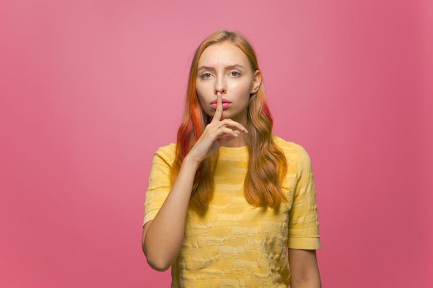 Mantieni il silenzio giovane ragazza adolescente moderna mostra gesto di silenzio tenendo il dito sulle labbra sullo studio rosa