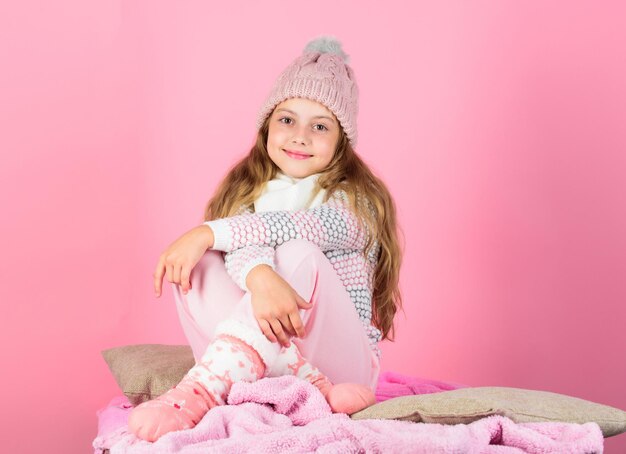 Mantieniti caldo e comodo. Accessori caldi che ti terranno al caldo questo inverno. Kid girl indossare berretto lavorato a maglia rilassante sfondo rosa. Il cappello di lana caldo dei capelli lunghi del bambino gode del caldo. Concetto di vestiti caldi.