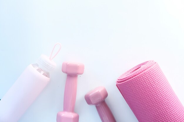 manubri di colore rosa, tappetino per esercizi e bottiglia d'acqua su uno spazio bianco