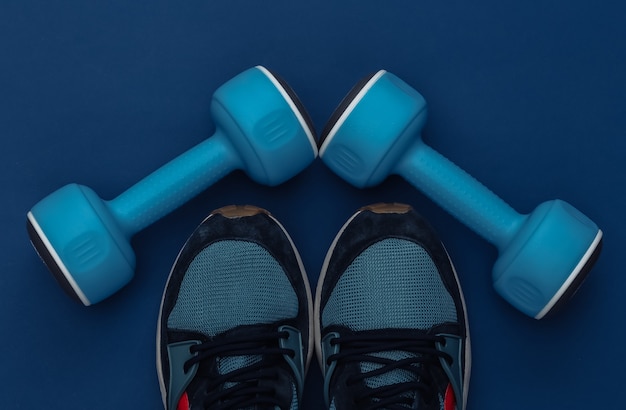 Manubri e scarpe da ginnastica su sfondo blu classico. Stile di vita sano, allenamento fitness. Colore 2020. Vista dall'alto