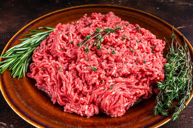 Manzo macinato crudo o carne di vitello su un piatto rustico con erbe aromatiche. Sfondo scuro. Vista dall'alto.