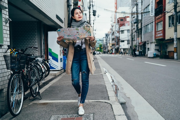 mappa di viaggio della holding del giovane turista a figura intera nella città di osaka in giappone. Donna che visita la visita alla ricerca di indicazioni sulla mappa di viaggio sulla strada giapponese urbana. viaggiatore femminile che cammina in molte biciclette.