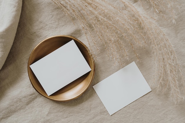Marchio bohémien di lusso estetico o modello di biglietti d'invito Foglio di biglietti d'invito in carta bianca con mock up vuoto spazio copia erba di pampa secca su panno di lino stropicciato beige neutro