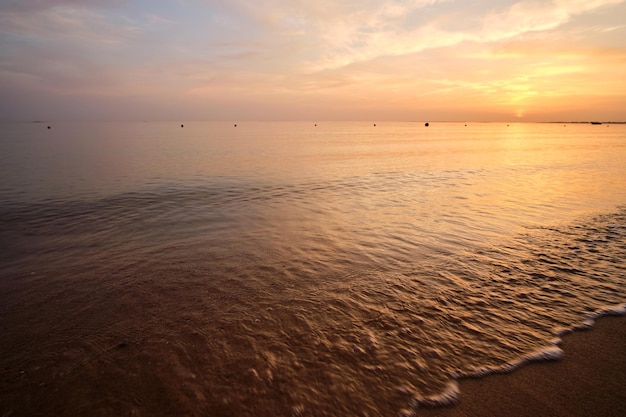 Mare calmo con onde che si infrangono sulla spiaggia sabbiosa all'alba.