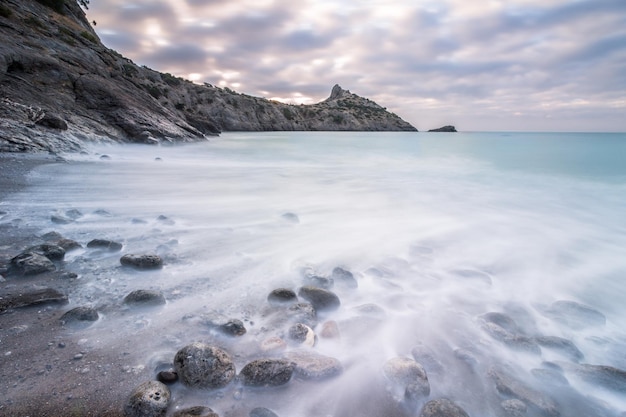 Mare mattutino, pietre e lungo mantello. Cielo nuvoloso.