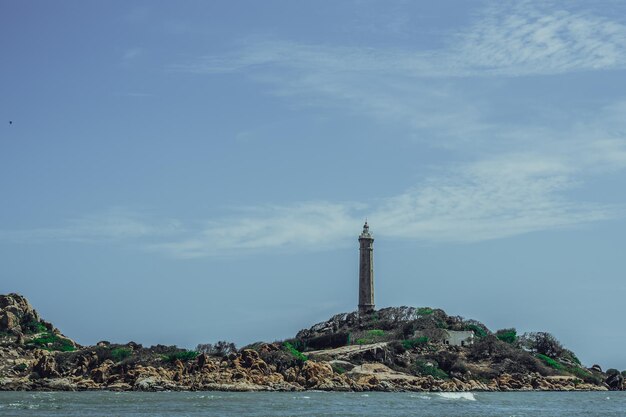 Mare natura vista panoramica paesaggio sfondo Oceano scogliere rocciose isola boscosa Cielo azzurro chiaro Faro sulla cima della montagna Segnale avvertire i marinai naufragio viaggio concetto speranza scopo della vita