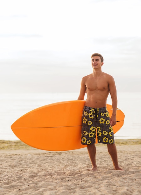 mare, vacanze estive, sport acquatici e concetto di persone - giovane sorridente con tavola da surf sulla spiaggia