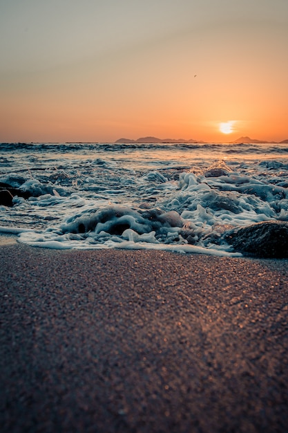 Maree che si infrangono sulla sabbia della spiaggia durante un tramonto