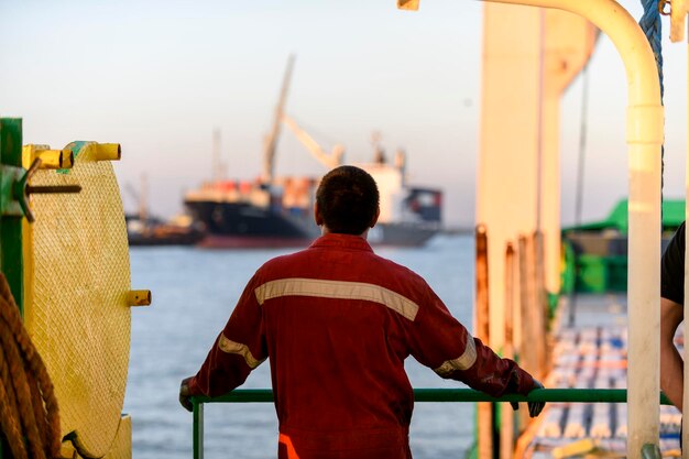 Marinaio in tuta da lavoro rossa e casco arancione sul ponte Lavorare in mare Nave da carico Operazioni di ormeggio Abile marinaio