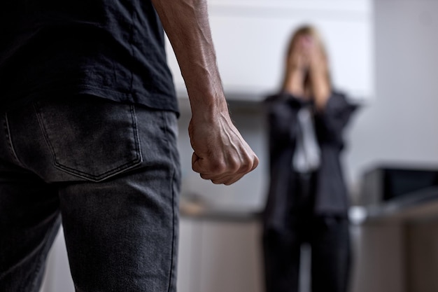 Marito aggressivo e arrabbiato che sta per battere la moglie piangente infelice in piedi sullo sfondo