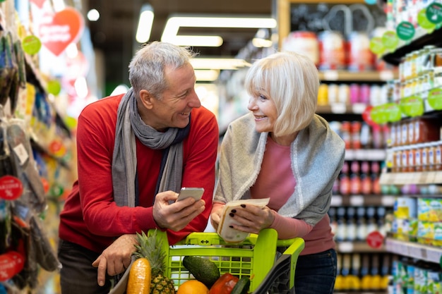 Marito e moglie anziani positivi che acquistano insieme utilizzando lo smartphone