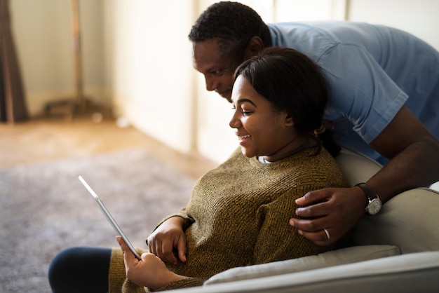 Marito e moglie di origine africana che riposano a casa, usando un tablet insieme