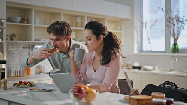 Marito in fretta per il lavoro a colazione con la moglie in cucina donna con il tablet