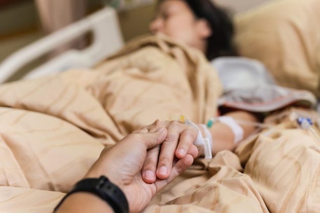 Marito mano che tiene la mano della moglie sul letto nella stanza d'ospedale