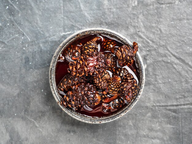 Marmellata deliziosa con le pigne del bambino in piccola ciotola. Dessert siberiano tradizionale con giovane marmellata di pigne su struttura grigia