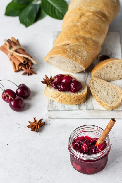 Marmellata di ciliegie con spezie (cannella, anice) con ciliegie fresche nei vasetti e pane.