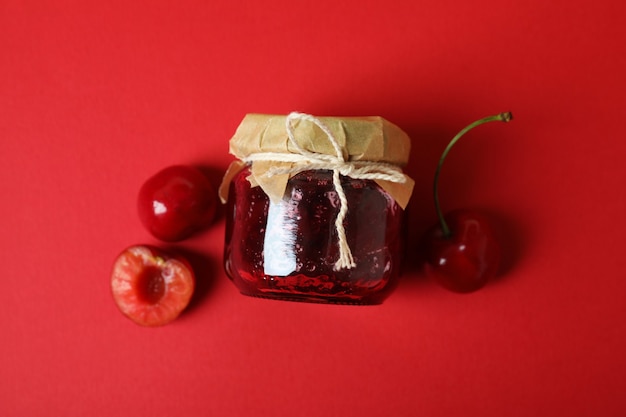 Marmellata di ciliegie e ingredienti su sfondo rosso