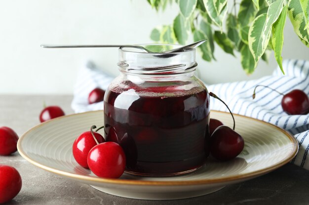 Marmellata di ciliegie e ingredienti sul tavolo grigio strutturato