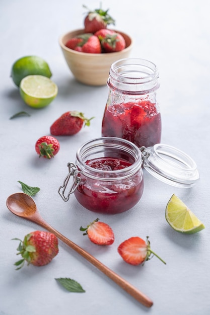 Marmellata di fragole fatta in casa Alimenti conservati in un barattolo di vetro con frutti di bosco biologici freschi su sfondo chiaro con lime