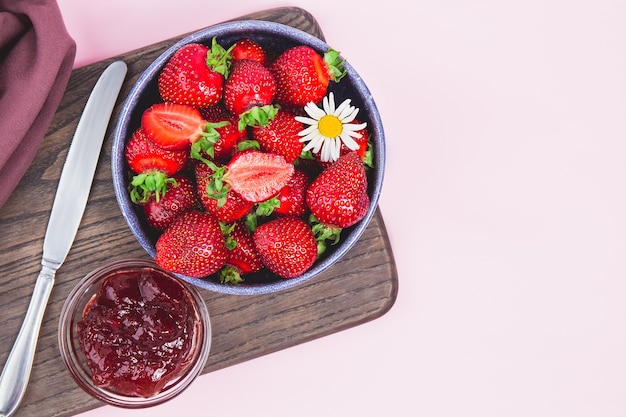 Marmellata di fragole fatta in casa o gelatina di fragole con fragole mature fresche su un piatto bianco. Colazione con pane tostato con marmellata di fragole. Coltello per spalmare la marmellata. Conserve estive.