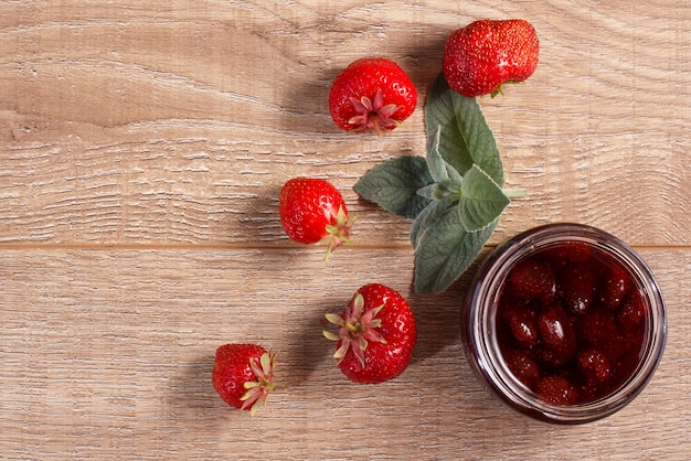 Marmellata di fragole fatta in casa tradizionale in un barattolo con fragole fresche su scrivania in legno Vista dall'alto