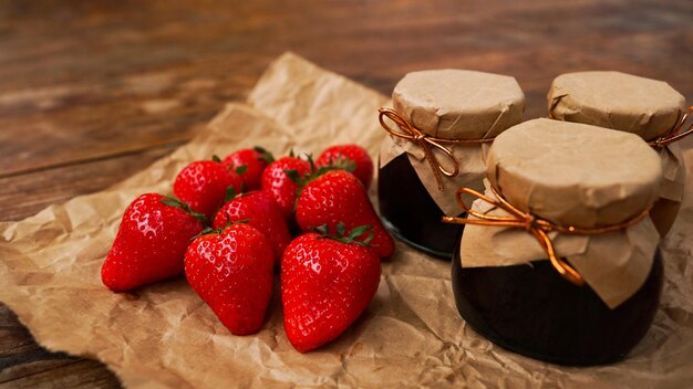 Marmellata di fragole nel barattolo di vetro con frutti di bosco freschi su fondo di legno