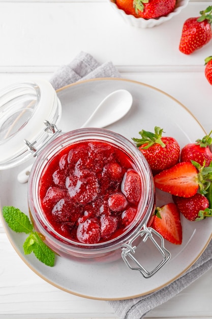 Marmellata di fragole nel barattolo di vetro con frutti di bosco freschi su un tavolo di legno bianco Dessert estivo Copia spazio