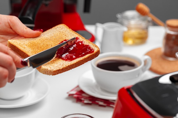 Marmellata di fragole spresding della mano femminile su pane tostato al forno