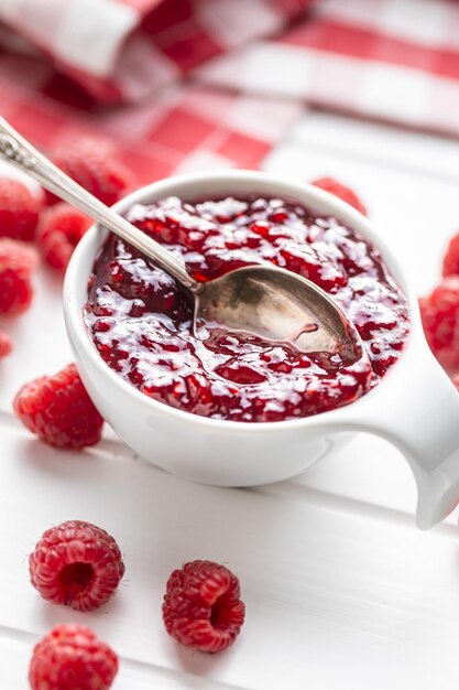 Marmellata di lamponi dolce in una ciotola e lamponi sul tavolo bianco