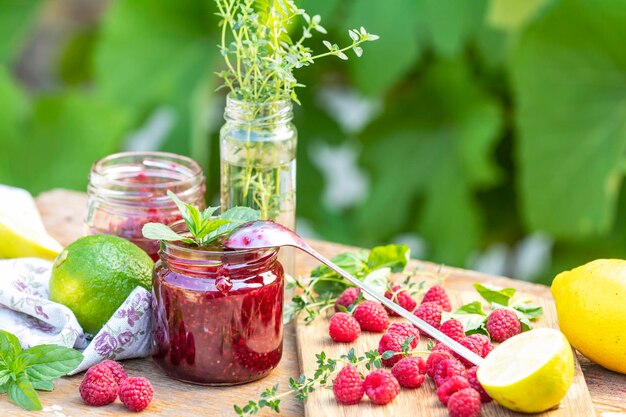 Marmellata di lamponi e lamponi freschi su un tavolo rustico in legno in giardino Giornata soleggiata estiva da vicino con profondità di campo ridotta