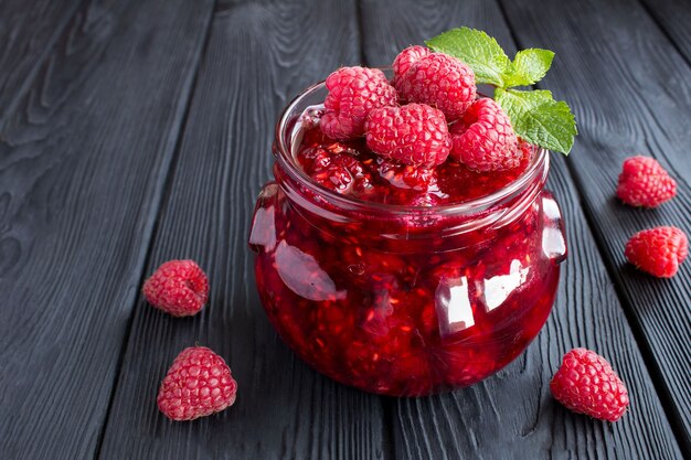 Marmellata di lamponi nel barattolo di vetro sul tavolo di legno nero