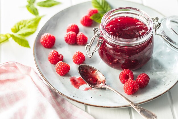 Marmellata di lamponi rossi in barattolo e lamponi maturi sul piatto