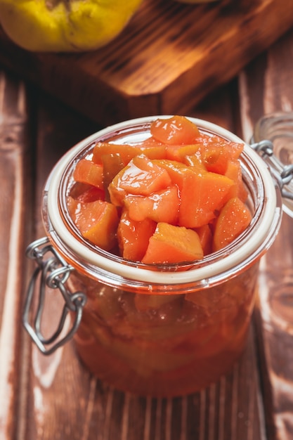 Marmellata di mele cotogne nel barattolo di vetro e frutta sullo sfondo