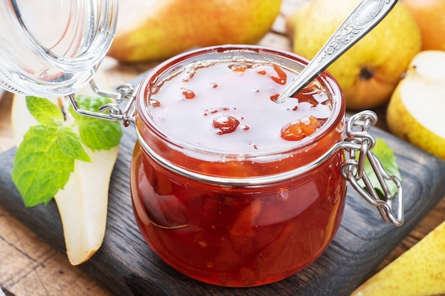 Marmellata di pere fatta in casa in un barattolo e pere fresche su uno sfondo di legno.