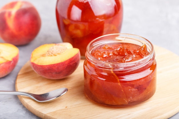 Marmellata di pesche in un barattolo di vetro con frutta fresca su sfondo grigio cemento. vista laterale.