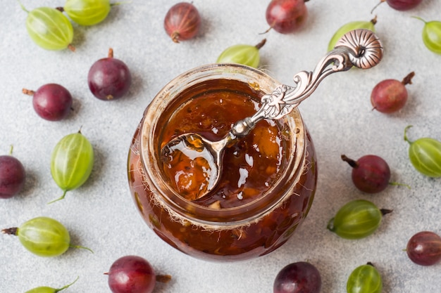 Marmellata di uva spina in un barattolo con bacche fresche di uva spina su una superficie grigia