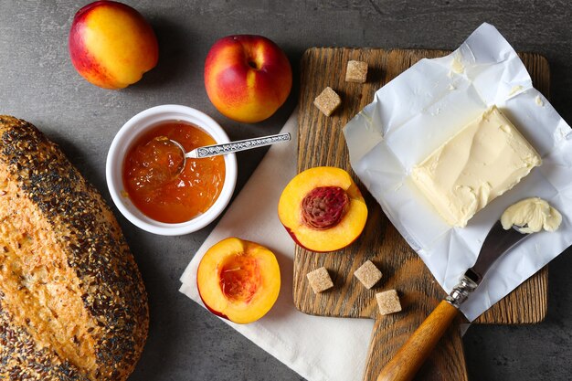 Marmellata saporita nella ciotola, pesche mature, burro, cracker e pane fresco sul primo piano della tavoletta di legno