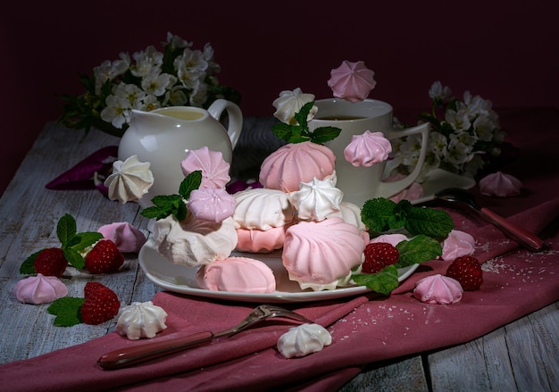 Marshmallow ariosi di colore bianco, rosa e lilla su un piatto bianco, un tovagliolo rosa scuro, con un lampone