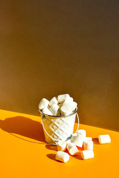 Marshmallow bianchi in un secchio di metallo su uno sfondo moderno giallo e grigio un ingrediente