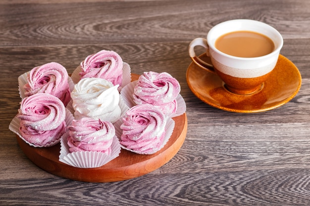 Marshmallow bianco e rosa (zephyr) su una tavola di legno rotonda con una tazza di caffè