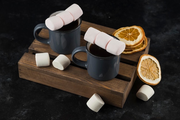 Marshmallow con caffè in tazza con arancia affettata secca sul piatto di legno di taglio