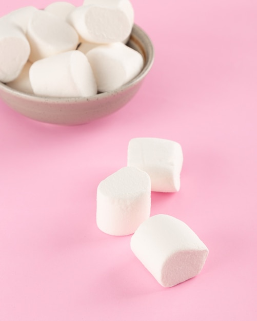 Marshmallow in ciotola su sfondo rosa pastello.