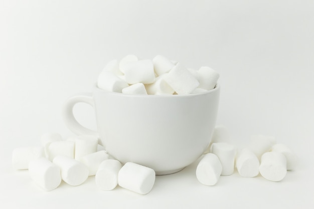 Marshmallow nella tazza sulla superficie bianca.