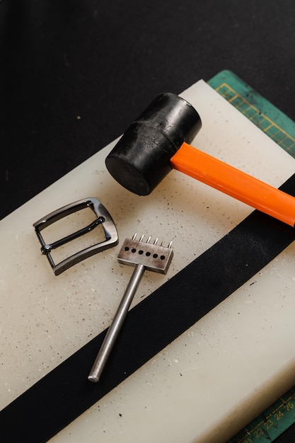 Martello con fibbia per cintura in vera pelle e punzone di linea Strumenti dell'artigiano per la creazione di cinture Attrezzatura per la produzione di cinture in vera pelle sul tavolo in officina